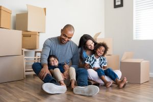Happy family with two children having fun at new home. Young multiethnic parents with two sons in their new house with cardboard boxes. Smiling little boys sitting on floor with mother and dad.
